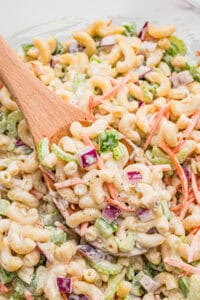 Spoonful of macaroni salad with elbow macaroni, shredded carrots, celery, green pepper, and red onion coated in creamy dressing.