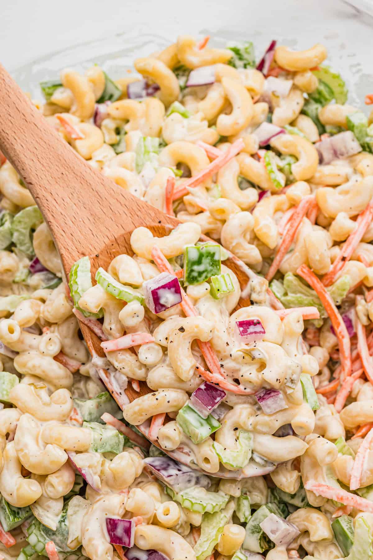 Spoonful of macaroni salad with elbow macaroni, shredded carrots, celery, green pepper, and red onion coated in creamy dressing.