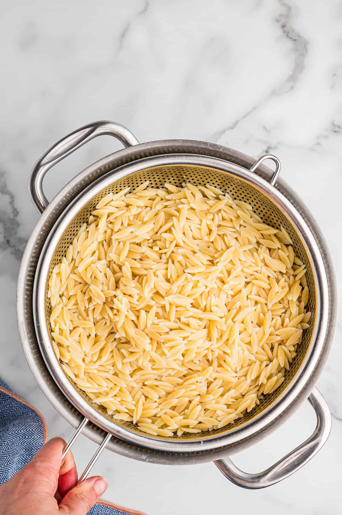 Cooked orzo pasta draining in a metal colander over a pot.