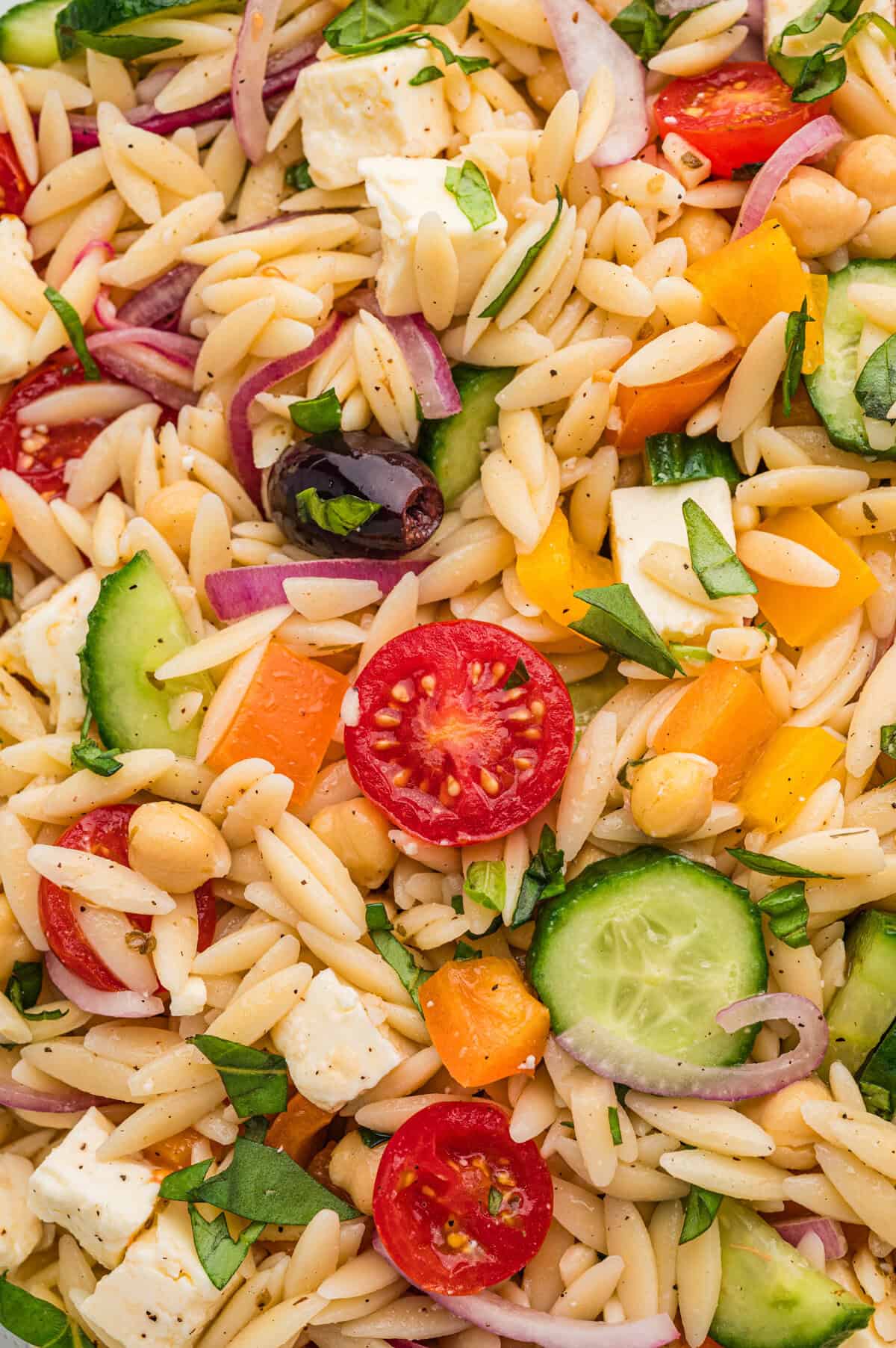 Extreme close-up of orzo salad showing detailed textures of vegetables and pasta.
