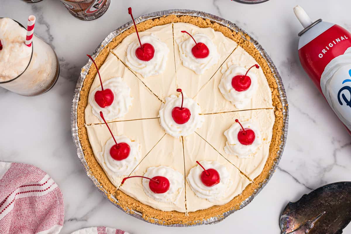 A whole frozen root beer float pie sliced into 8 pieces, each topped with whipped cream and a maraschino cherry.