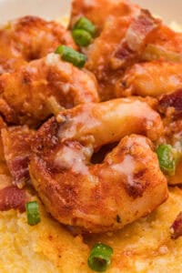 Saucy, seasoned shrimp resting on creamy yellow grits, with visible pieces of green onion and bacon.