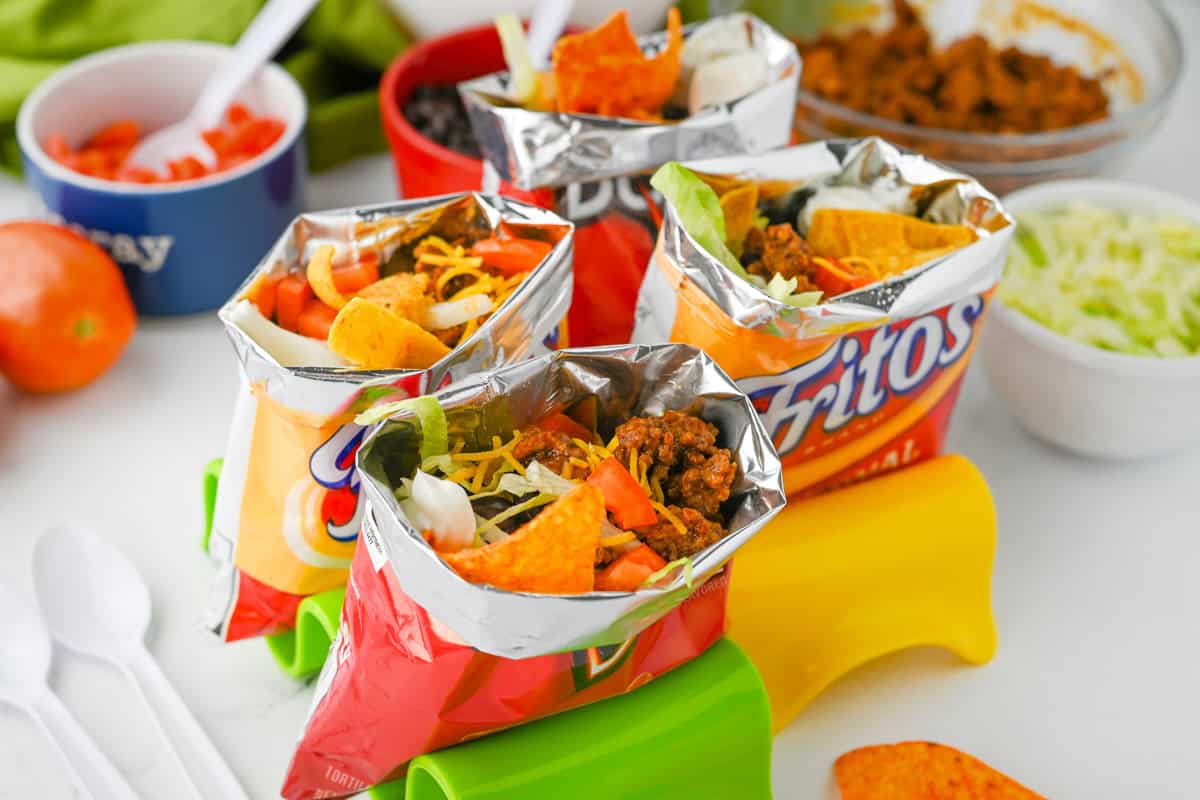 Several walking tacos in chip bags with toppings.