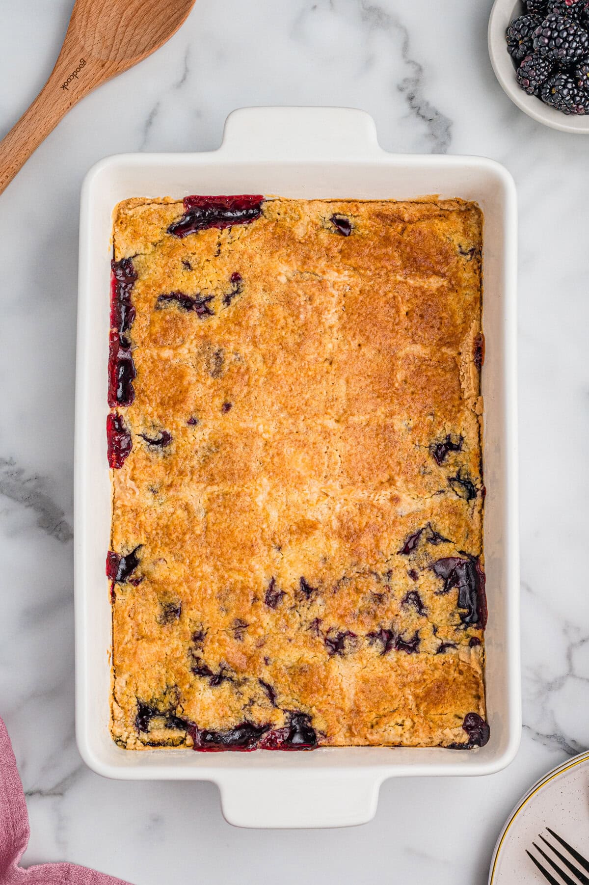 Blackberry dump cake in a 9x13 baking dish with a golden-brown top and patches of dark purple berry filling visible around the edges.