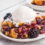 Blackberry dump cake topped with vanilla ice cream on a white plate.