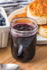 Jar of blueberry jam in front of a plate of biscuits.