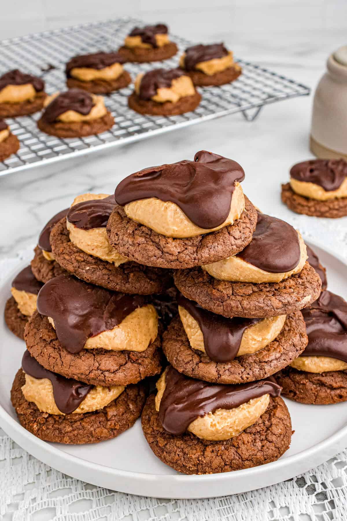 Plate stacked with peanut butter buckeye cookies, chocolate brownie cookies topped with a dollop of creamy peanut butter filling and covered partially with a smooth layer of chocolate ganche.
