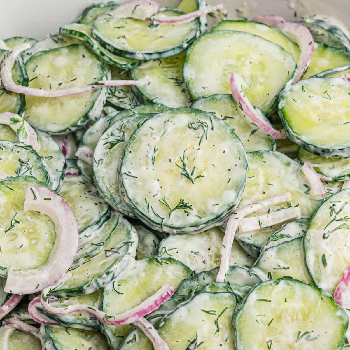 Creamy cucumber dill salad with thin cucumber slices, red onion, and chopped dill in a creamy white dressing.