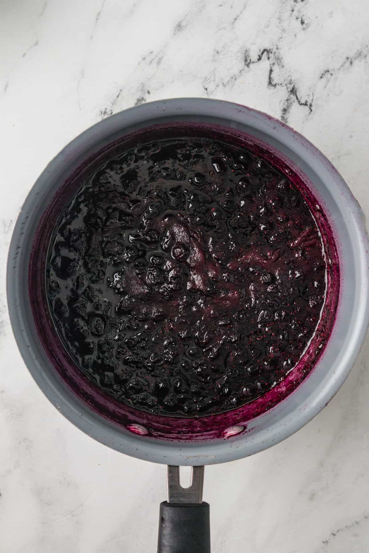 Overhead view of blueberry jam cooking in a saucepan. The jam appears thick with visible whole berries.