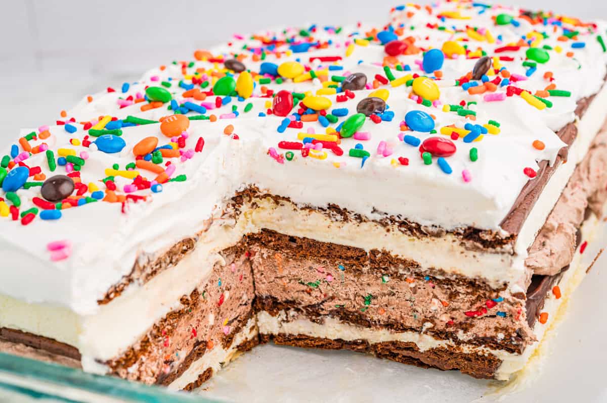 A layered ice cream sandwich cake topped with cool whip and rainbow sprinkles.