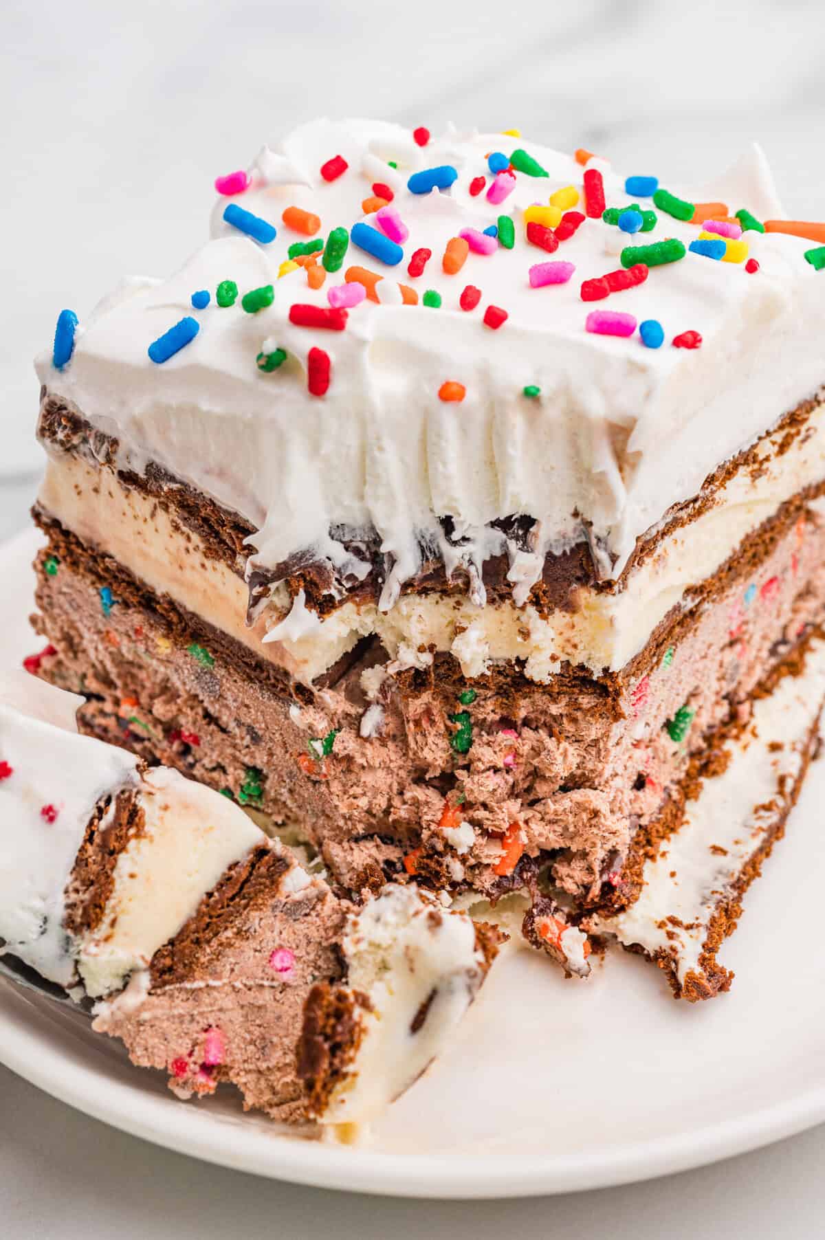 Partially eaten slice of ice cream sandwich cake with whipped topping and sprinkles.