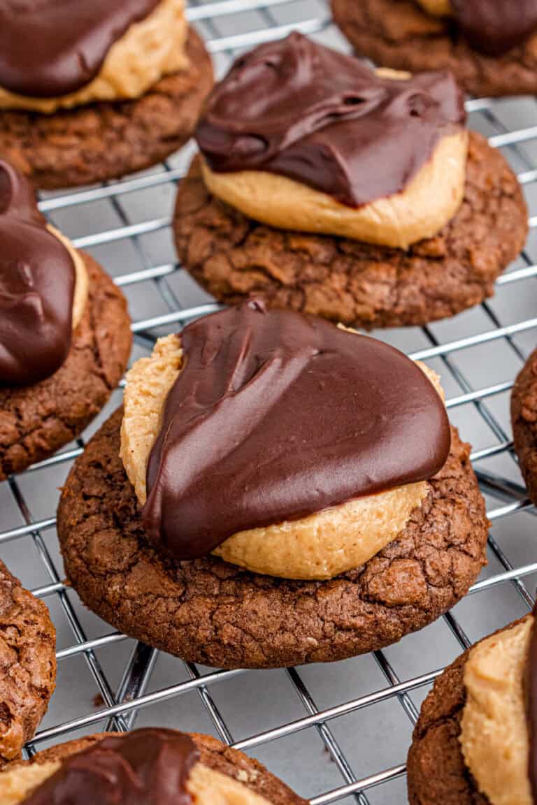 Close-up of buckeye cookies topped with a thick peanut butter layer and chocolate ganache on cooling rack,