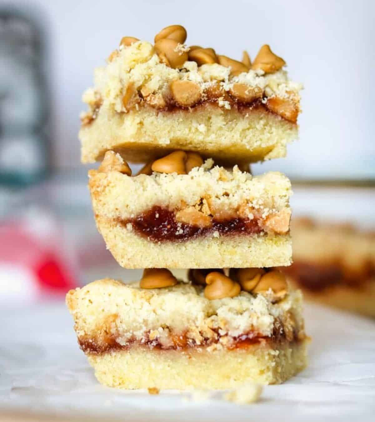 Peanut butter and jelly cookie bars with peanut butter chips and a layer of jam spread between two butter cookie layers.
