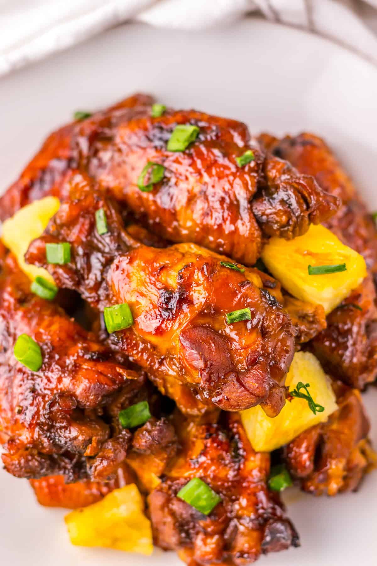 Close-up of glazed crockpot Hawaiian chicken wings, topped with bright yellow pineapple chunks and sprinkled with chopped green scallions.