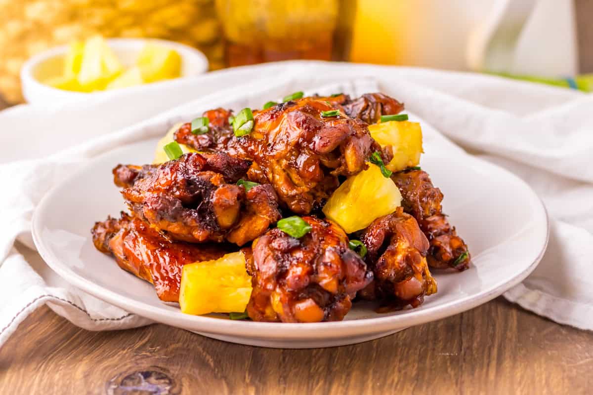 Hawaiian chicken wings on a white plate, featuring a glossy, dark glaze and garnished with pineapple chunks and chopped scallions.