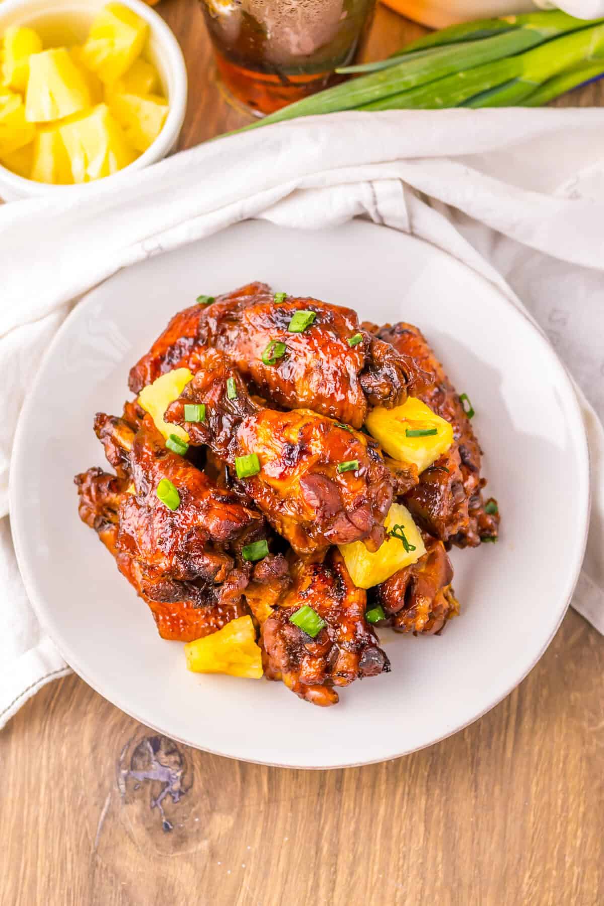 Overhead photo of a plate filled with slow cooker Hawaiian pineapple chicken wings garnished with pineapple chunks and green scallions.