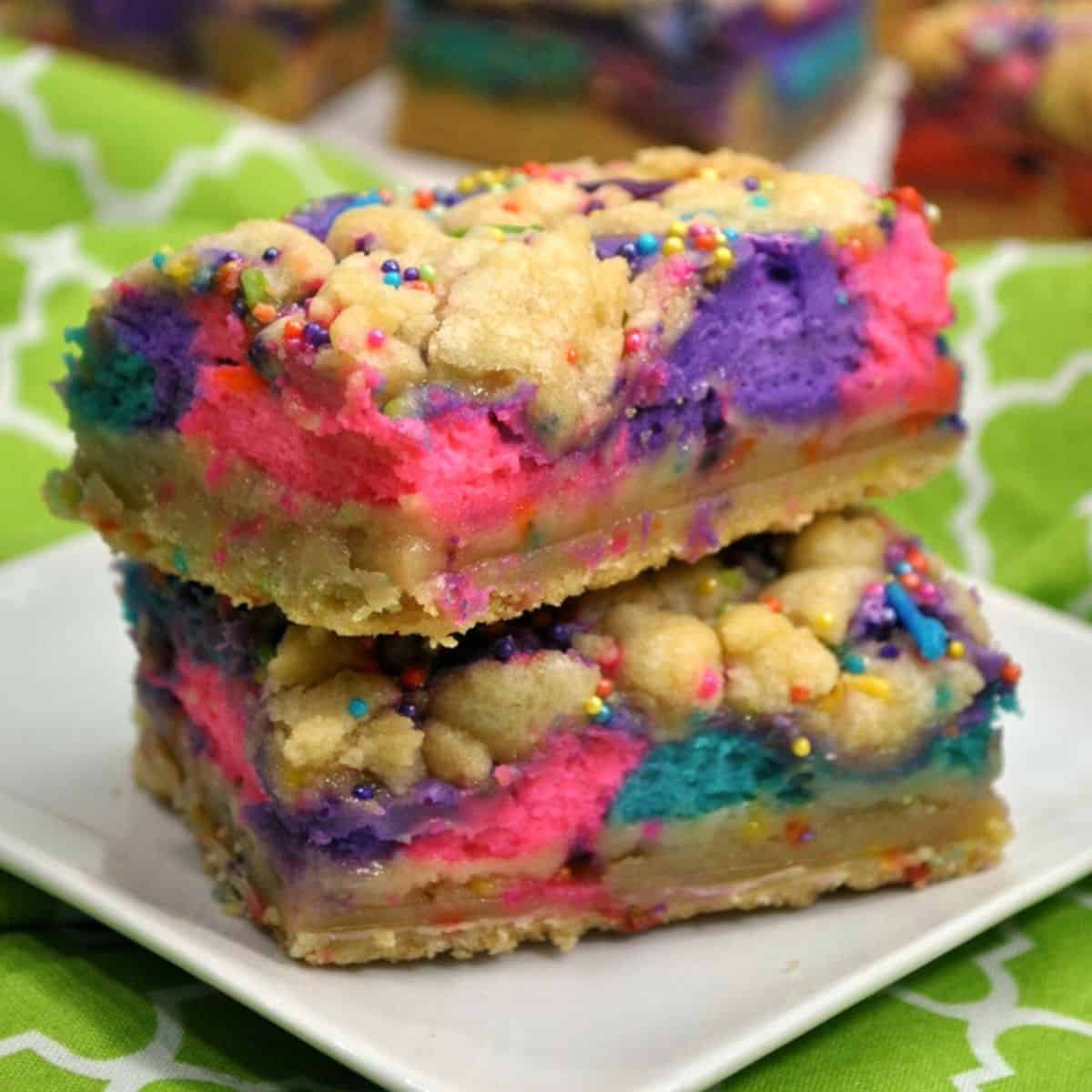 Two colorful layered dessert bars with bright pink, purple, and blue cheesecake swirls and cookie crumbles on top.