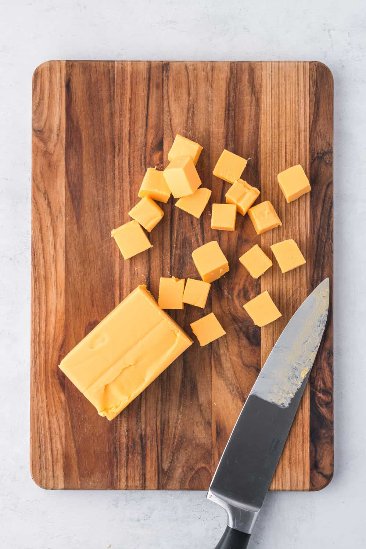 Cubes of velveeta cheese on cutting board next to a a block of velveeta and a knife.