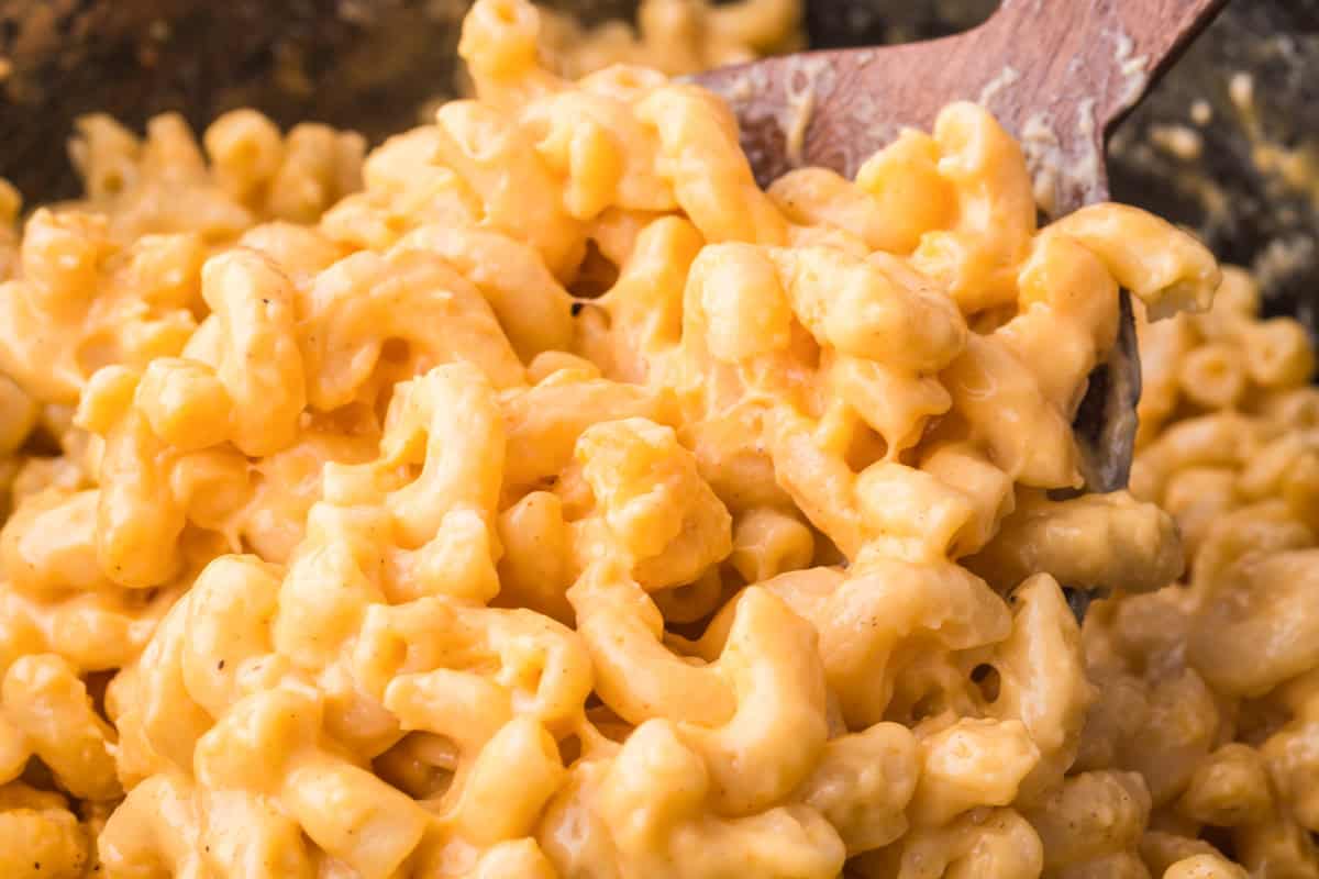 Close-up of creamy mac and cheese being scooped with a wooden spoon from a slow cooker.