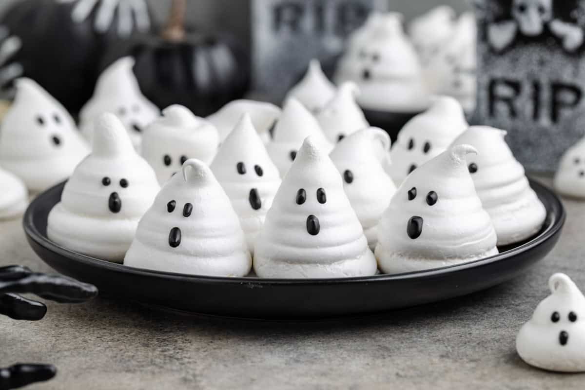 Ghost meringues on a plate with Halloween decorations in the background.