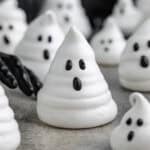 Ghost meringue cookie with a black gloved hand reaching toward it.Ghost meringue in foreground with a black gloved hand reaching toward it. More ghost meringues are in the background.
