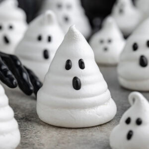 Ghost meringue cookie with a black gloved hand reaching toward it.Ghost meringue in foreground with a black gloved hand reaching toward it. More ghost meringues are in the background.