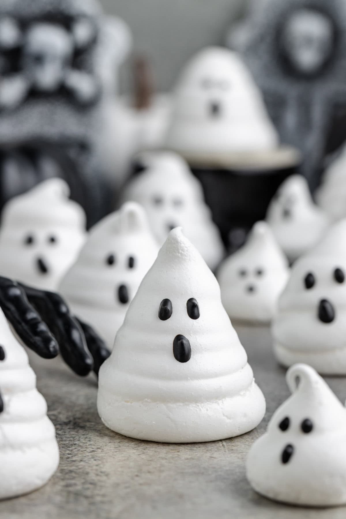 Ghost meringue cookie in foreground with a black gloved hand reaching toward it.Ghost meringue in foreground with a black gloved hand reaching toward it. More ghost meringues are blurred in the background.