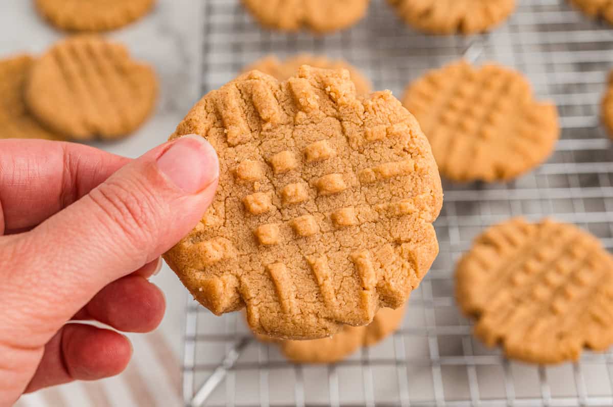 Hand holding a peanut butter cookie over a cooling rack.