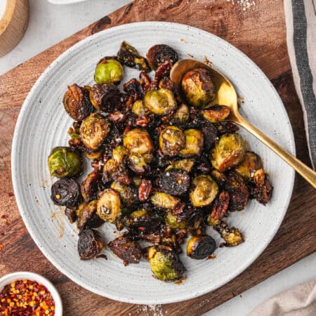 A plate filled with caramelized Brussels sprouts and pecans, sprinkled with seasoning. A gold spoon rests in the dish.
