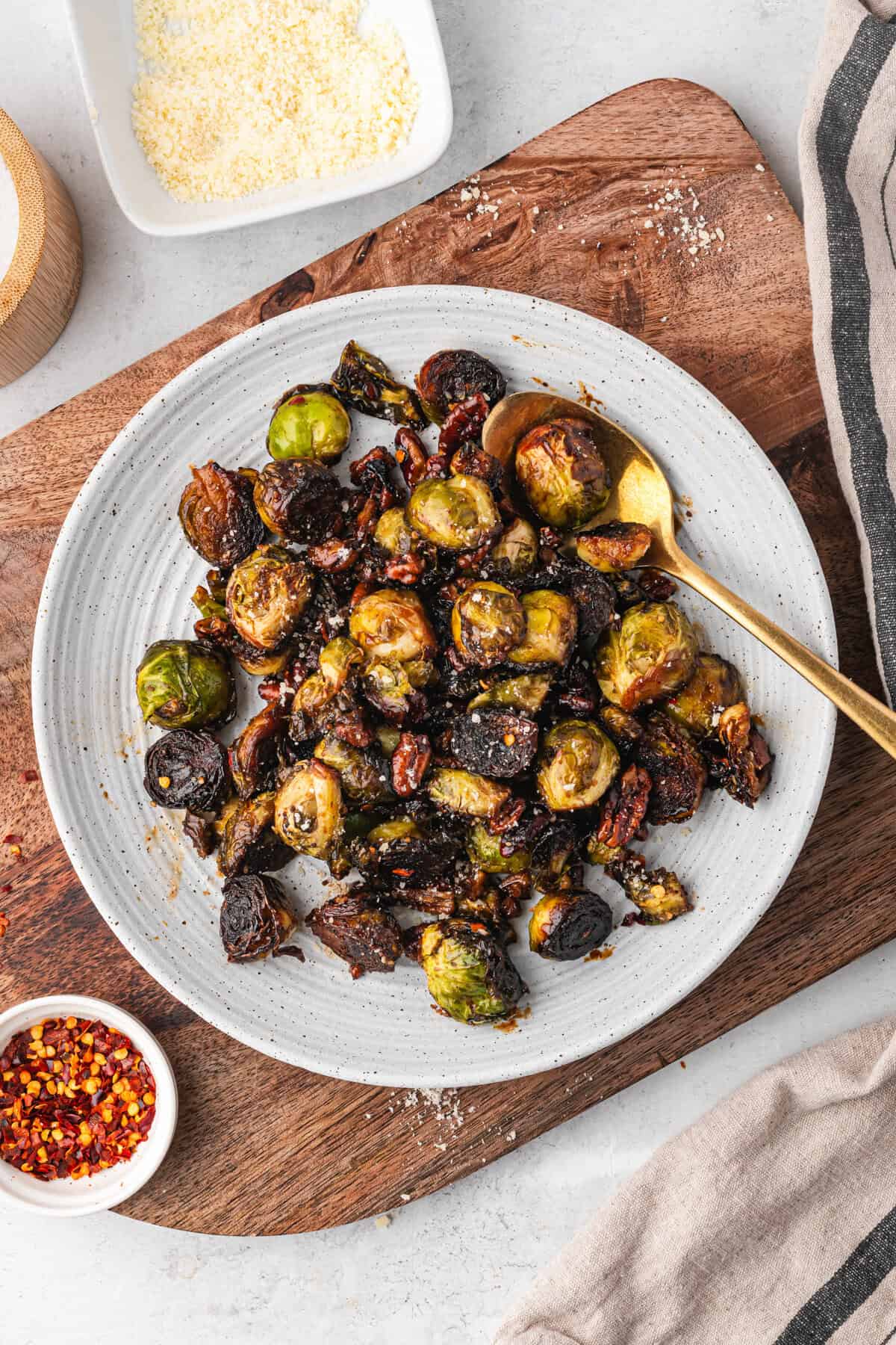 A plate filled with caramelized Brussels sprouts and pecans, sprinkled with seasoning. A gold spoon rests in the dish.