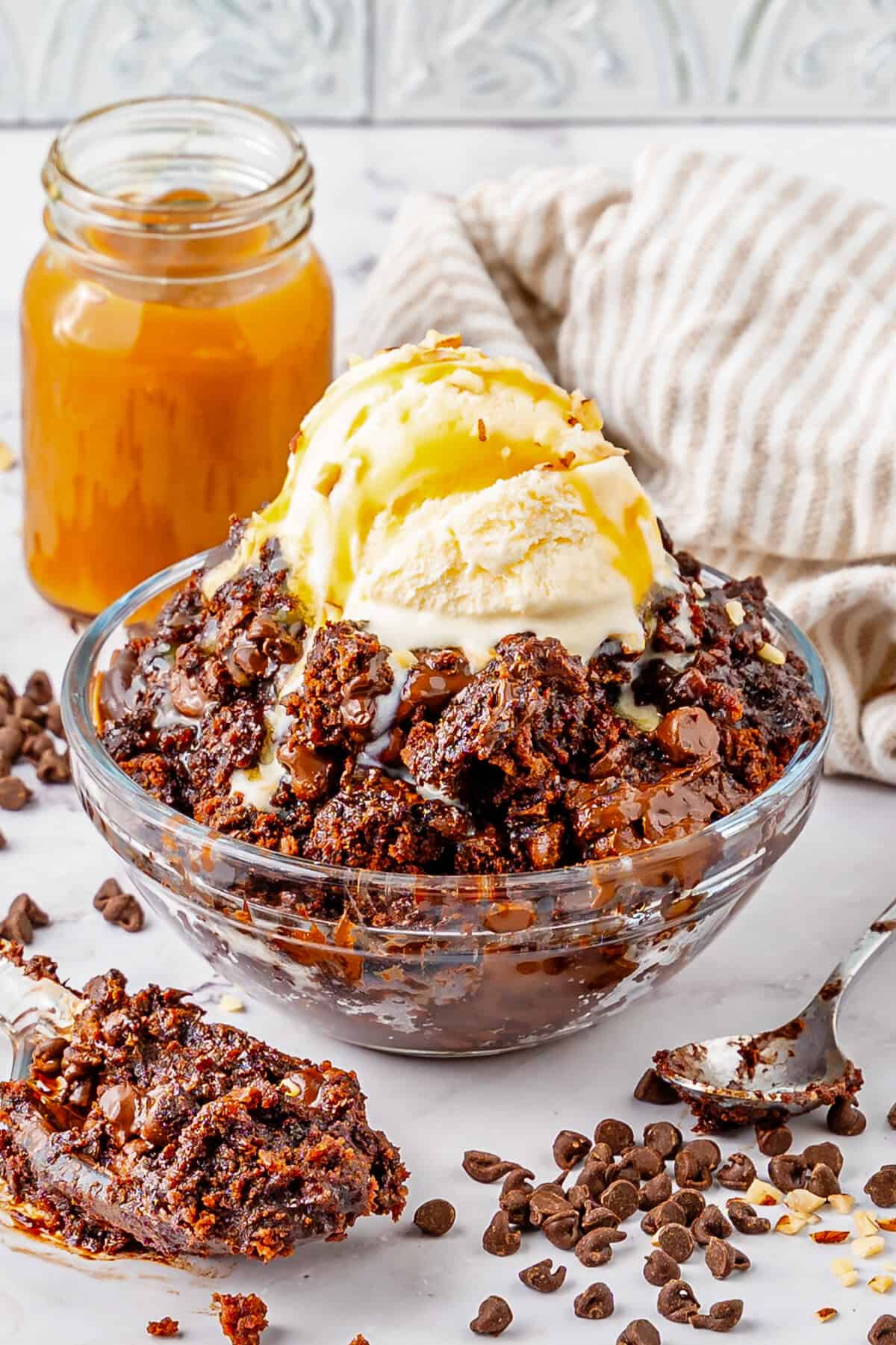 Chocolate dump cake in a bowl with ice cream and caramel drizzle.