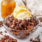 Bowl of chocolate dump cake with chocolate chips, chocolate syrup, and scoop of vanilla ice cream.