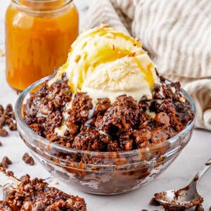 Bowl of chocolate dump cake with chocolate chips, chocolate syrup, and scoop of vanilla ice cream.