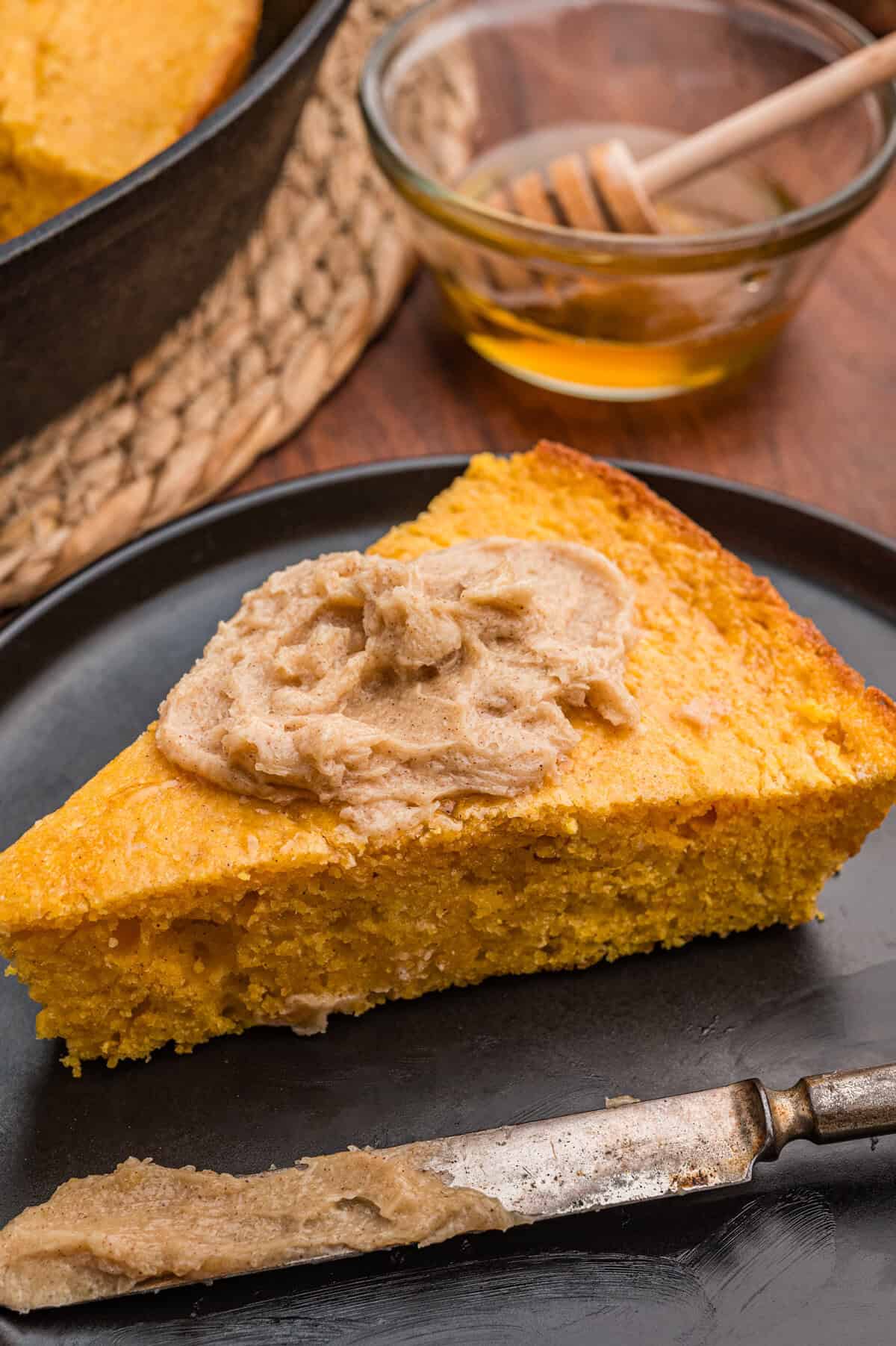 Slice of sweet potato cornbread topped with cinnamon butter spread on a black plate.