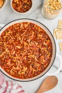 Overhead view of a large pot of hamburger noodle soup with ground beef, egg noodles, vegetables, and a tomato-based broth.