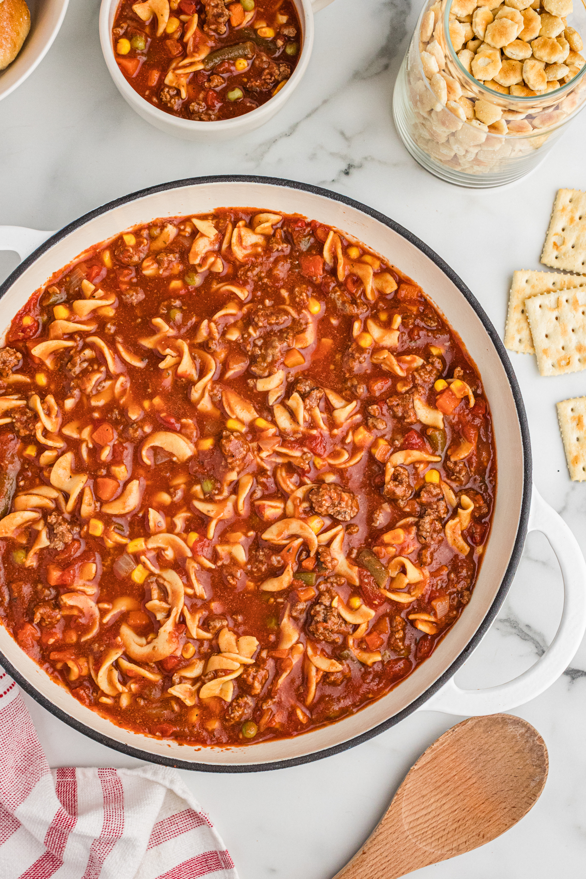 Overhead view of a large pot of hamburger noodle soup with ground beef, egg noodles, vegetables, and a tomato-based broth.