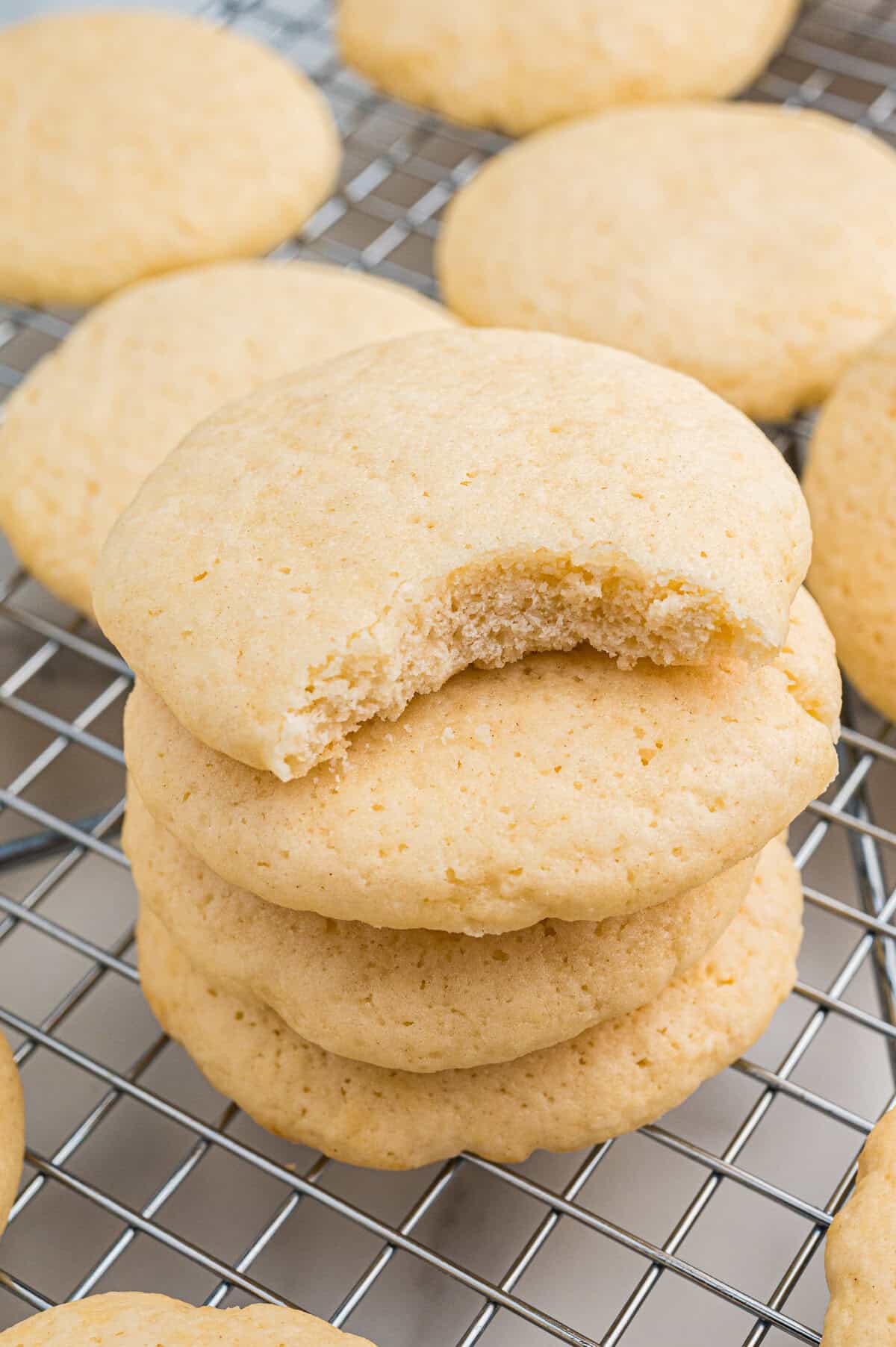 Stack of old-fashioned tea cakes on a wire cooling rack. The top cookie has a visible bite taken from it, revealing its soft, cakey interior.