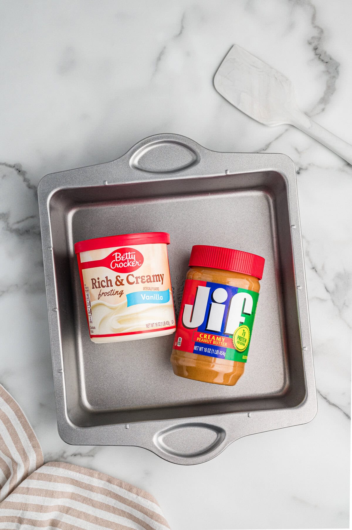 Overhead view of a baking pan containing a jar of Jif creamy peanut butter and a container of Betty Crocker Rich & Creamy vanilla frosting.