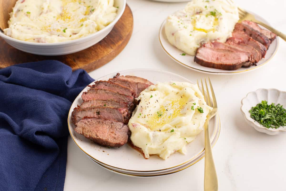 Plate of red skinned mashed potatoes with sliced beef.