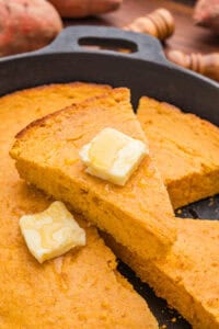 Several slices of sweet potato cornbread in a cast iron skillet with melting butter and honey drizzled on top.