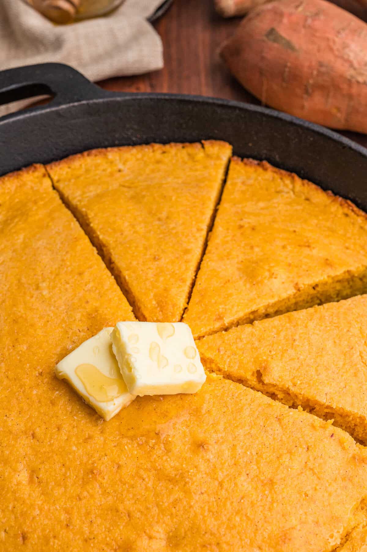 Close-up of sweet potato cornbread wedges topped with butter and honey.