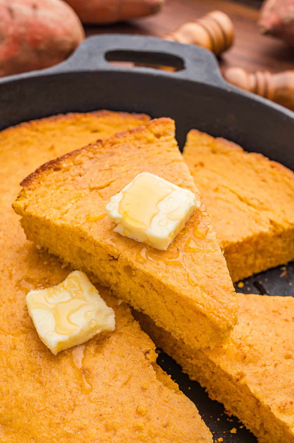 Several slices of sweet potato cornbread in a cast iron skillet with melting butter and honey drizzled on top.