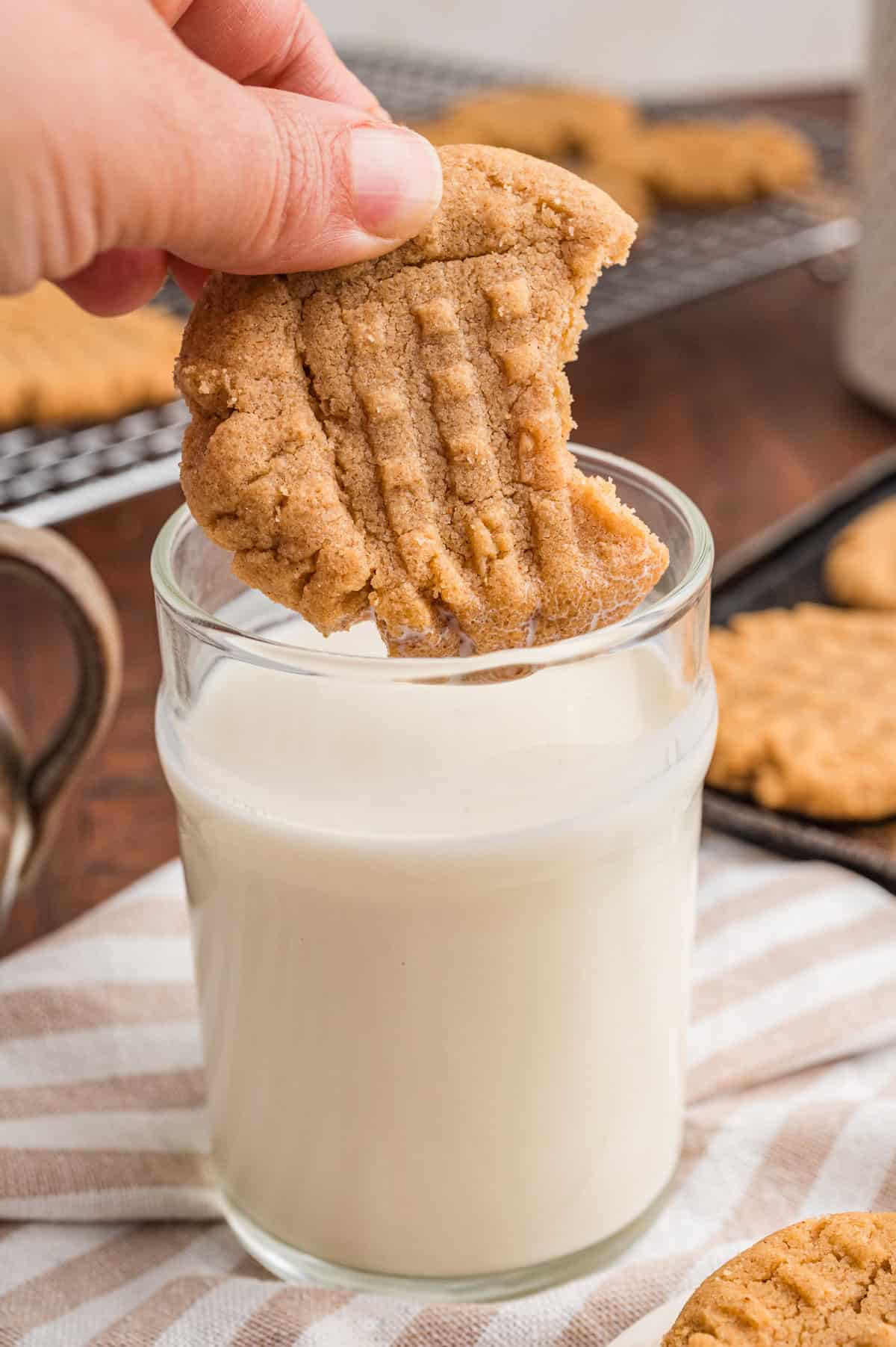 Hand dipping a peanut butter cookie into a glass of milk.
