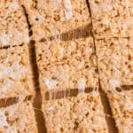Top-down close-up of cut brown butter Rice Krispie treat squares on parchment paper, with melted marshmallows stretching between the pieces.