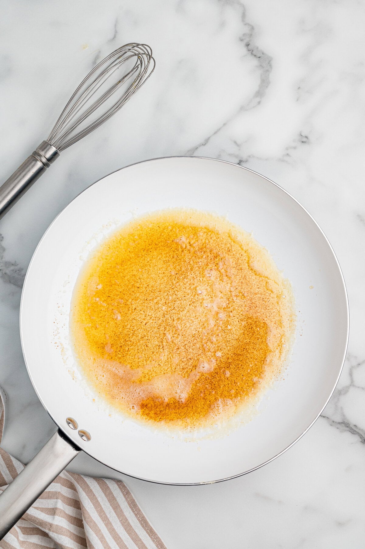 Melted browned butter in a white skillet with metal whisk nearby.