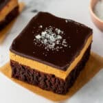 A buckeye brownie with three layers: a chocolate brownie base, a thick peanut butter layer, and a smooth chocolate ganache topping sprinkled with flaky sea salt.