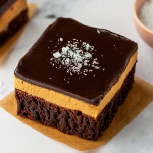 A buckeye brownie with three layers: a chocolate brownie base, a thick peanut butter layer, and a smooth chocolate ganache topping sprinkled with flaky sea salt.