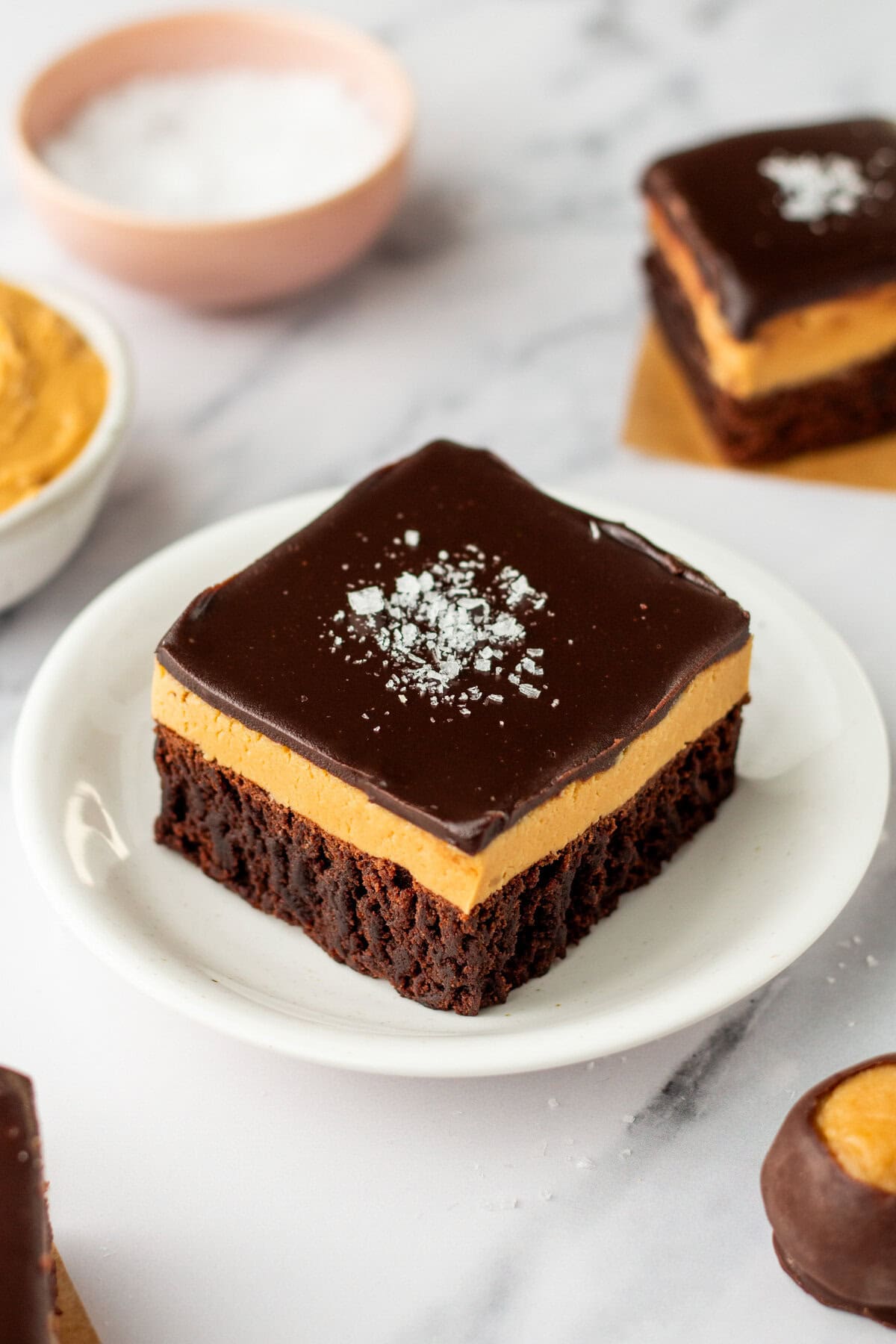 A buckeye brownie with three layers: a chocolate brownie base, a thick peanut butter layer, and a smooth chocolate ganache topping sprinkled with flaky sea salt.