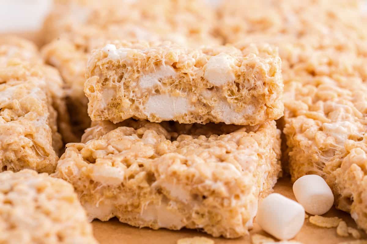 Close-up of a single gooey brown butter Rice Krispie treat resting on top of other cut squares, showing detailed texture and visible melted marshmallow strands.