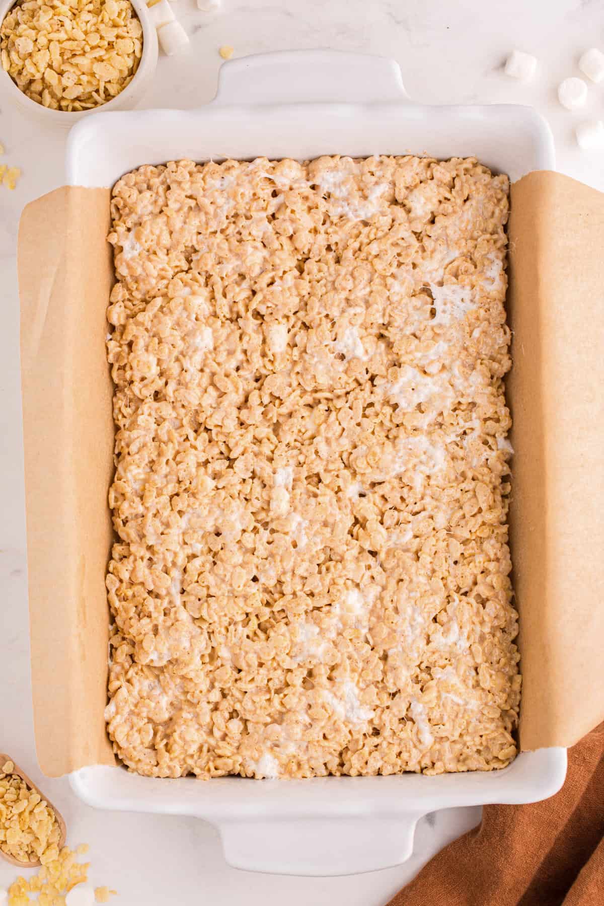 Uncut Rice Krispie treat mixture pressed into a parchment-lined dish.